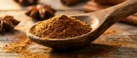Ground cinnamon powder in wooden spoon with star anise and cinnamon sticks on rustic wood background for cooking and baking recipes.