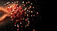 Explosive burst of pink Himalayan salt crystals and red peppercorns against black background with dynamic motion and scattered spice particles.