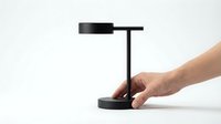 Minimalist black desk lamp with sleek modern design, touched by a hand, isolated on white background for interior and product design use.