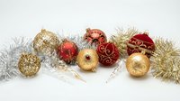 Festive Christmas ornaments in red and gold with silver tinsel garland arranged on white background for holiday decorating and seasonal celebrations.