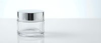 Empty glass cosmetic jar with silver lid on white background isolated for skincare product packaging and beauty brand design.