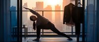 Young athletic woman performing side plank exercise on high-rise apartment balcony at sunrise, urban skyline background, fitness and wellness lifestyle content.
