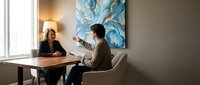 Professional business meeting between diverse colleagues discussing strategy in modern office with abstract blue artwork on wall.