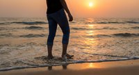 Woman standing in ocean waves at sunset beach with golden light reflecting on water creating peaceful moment for relaxation and mindfulness meditation.