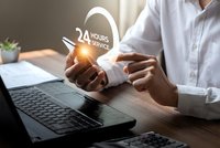 Professional businessman holding glowing 24 hours service icon above laptop computer in modern office workspace representing customer support and assistance.