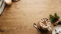 Overhead view of warm mug with marshmallows and hot chocolate on wooden table with evergreen branches and candle for winter holiday beverage styling and seasonal marketing.