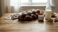 Freshly baked chocolate donuts dusted with powdered sugar on rustic wooden table with milk bottle. Cozy kitchen morning scene for bakery advertising.