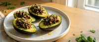 Halved avocados topped with seasoned ground meat mixture and fresh herbs, served on white plate for healthy lunch or dinner meal preparation.