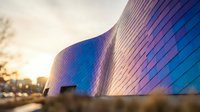 Modern curved glass facade with blue and purple LED lighting illuminating architectural exterior at dusk, suitable for corporate, technology, and contemporary design projects.