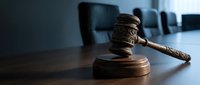 Wooden judge gavel on courtroom table with blurred chairs in background for legal proceedings and justice system concepts.