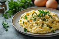Creamy scrambled eggs garnished with fresh parsley on ceramic plate, served with herbs and spices. Rustic breakfast setting with natural light.