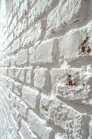 White painted brick wall with rough textured surface and exposed areas showing original red brick underneath, photographed at an angle creating depth perspective.