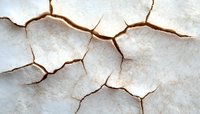 Cracked dry earth texture with deep brown fissures on white surface creates natural abstract pattern for environmental or drought concept backgrounds.