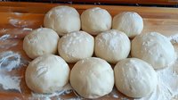 Fresh raw dough balls dusted with flour arranged in rows on wooden surface, ready for baking bread, pizza or pastries. Homemade cooking preparation process.