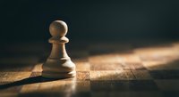 Single wooden chess pawn piece standing alone on rustic wood surface with dramatic lighting and dark background for strategy and leadership concepts.