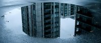 Modern apartment buildings reflected in urban puddle water after rain, creating mirror effect for real estate and city development concepts.