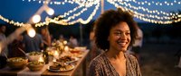 Young African American woman smiling at outdoor dinner party with string lights and festive table setting during evening celebration gathering.