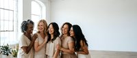 Diverse group of happy women friends embracing in bright white studio space with natural light from large windows for lifestyle photography.