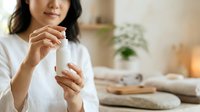 Young woman of East Asian descent applying hand cream or lotion in a bright, minimalist home interior with natural light, wellness and skincare routine.