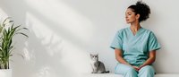 Young African American female healthcare worker in scrubs sitting on floor with gray cat, sunlight casting shadows through window, minimalist medical setting.