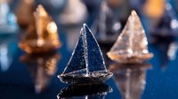 Miniature crystal and metallic sailboat figurines arranged on reflective dark blue surface creating dreamy nautical display with selective focus on central boat.