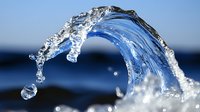 Crystal clear water splash forming elegant arc against blue sky background with droplets frozen in motion creating dynamic fluid movement.