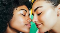 Two diverse young women with closed eyes touching foreheads in intimate moment showing friendship, love and connection against bright green background.