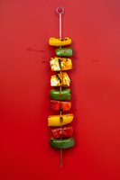 Grilled vegetable and tofu kebab with colorful bell peppers on metal skewer against vibrant red background, food photography for restaurant menu or cooking blog.