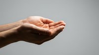 Open palm of a person with medium skin tone against neutral gray background, suitable for concepts of giving, receiving, charity, support, care, and generosity.