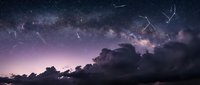 Spectacular meteor shower streaking across starry night sky with Milky Way galaxy visible above dramatic cloud formations creating cosmic celestial display.