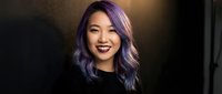 Young Asian woman with purple hair smiling confidently in modern indoor setting. Professional portrait with warm lighting for lifestyle and business content.