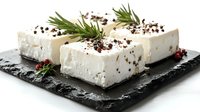 Creamy white cheese blocks topped with peppercorns and fresh rosemary sprigs arranged on a dark slate serving board, perfect for gourmet food photography and culinary content.