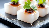 White cubed scallops topped with spicy sauce and fresh cilantro garnish served on black slate plate, close up view of gourmet Asian fusion appetizer.