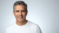 Confident middle-aged Hispanic man with gray hair wearing white t-shirt smiling at camera on light background for business and lifestyle content.