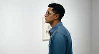 Young man with dark hair and glasses wearing a blue denim shirt, shown in profile against a white wall background. Suitable for business, lifestyle, and portrait projects.
