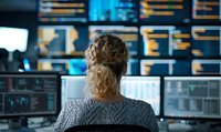 Female trader analyzing financial market data on multiple screens in dark office setting. Rear view of blonde woman monitoring stock exchange charts and graphs.