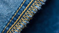 Close-up macro shot of frayed denim fabric edge with orange stitching and loose threads. Perfect for fashion, textile, and clothing design projects.