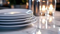 Stack of clean white porcelain plates on marble table with glowing candles creating romantic atmosphere, soft bokeh lights in background for dining setup.