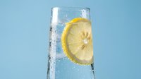 Refreshing glass of cold water with lemon slice and ice cubes on blue background, perfect for beverage, wellness, and hydration marketing.