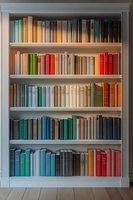 Elegant white bookshelf with colorful hardcover books arranged by hue, creating a rainbow effect across five shelves in a modern home library.