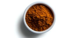 Ground turmeric powder in white ceramic bowl on white background, top view. Vibrant orange spice with rich texture and natural shadows creates striking contrast.