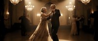 Elegant couple dancing at formal wedding reception in grand ballroom with crystal chandeliers and warm golden lighting, groom in tuxedo and bride in white gown.