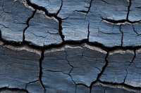 Dramatic close-up of dark cracked earth texture showing deep fissures and geometric patterns. Natural abstract background with rough surface and dried mud formation.