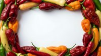 Colorful hot chili peppers arranged in circular frame on white background creating spicy food border for cooking and culinary design projects.
