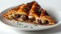 Flaky golden pastry filled with seasoned ground meat and melted cheese, garnished with fresh herbs on white plate. Savory homestyle baked dish.