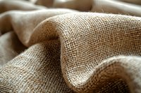 Natural burlap fabric with visible textile weave structure in warm beige tones creates organic waves and folds, showing detailed texture and shadows.