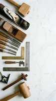 Vintage woodworking tools collection with chisels, planes, mallets and measuring instruments arranged on white marble surface for craftsmanship projects.
