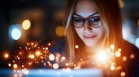 Young woman with glasses smiling while using laptop at night with warm bokeh lights creating magical atmosphere for technology and digital lifestyle concepts.
