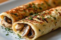 Savory crepes filled with mushrooms and herbs, garnished with fresh parsley on white plate. Close-up macro shot shows delicate texture and golden brown sear marks.