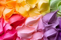 Colorful rainbow frosting swirls in vibrant gradient from orange and yellow to pink, purple and green, creating smooth decorative texture for cake design and food art.